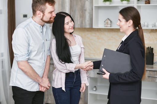 A young couple shakes hands with a real estate agent during a home tour or negotiation in a modern setting.
